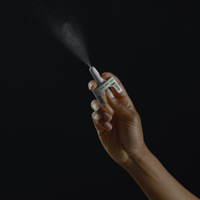 Close-up image of a person's hand squeezing the Opvee nasal spray used to reverse opioid overdoses.