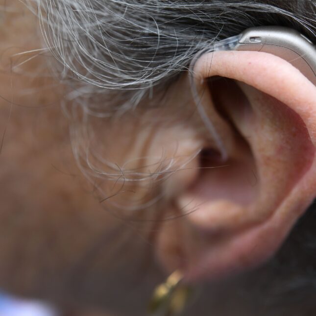 Photograph of a hearing aid in an older woman's ear – health tech coverage from STAT