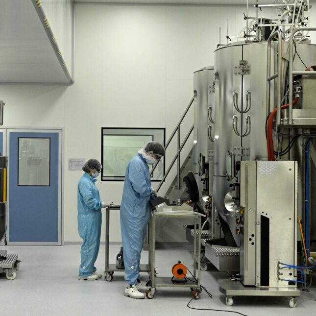 Two people in protective equipment work in a lab.