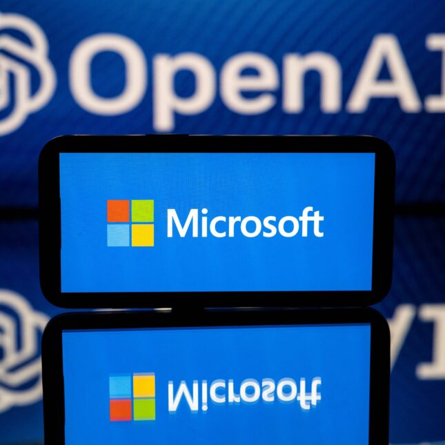 a phone screen display Microsoft's logo in front of a background projection of OpenAI's logo – health tech coverage from STAT